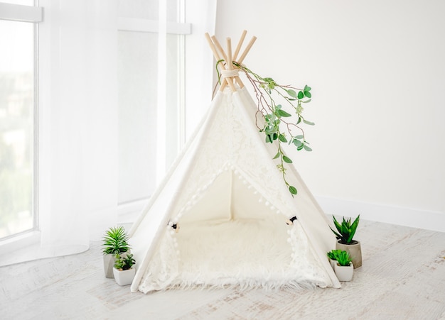 Hermosa decoración de cabaña blanca para sesión fotográfica de recién nacido con plantas y pieles en habitación luminosa. Wigwam de muebles con estilo para foto de estudio infantil infantil