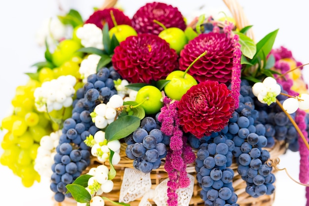 Hermosa decoración composición floral o ramo de frutas de temporada manzanas verdes y uvas con flores de crisantemo púrpura en canasta de paja aislado sobre fondo blanco.