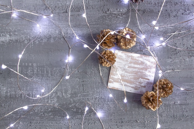 Hermosa decoración navideña en tonos plateados dorados conos de pino luces de año nuevo y tarjeta en blanco sobre un concreto ...