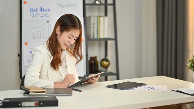 Hermosa directora ejecutiva corporativa con ropa informal inteligente viendo una presentación en línea en una tableta digital en una oficina moderna