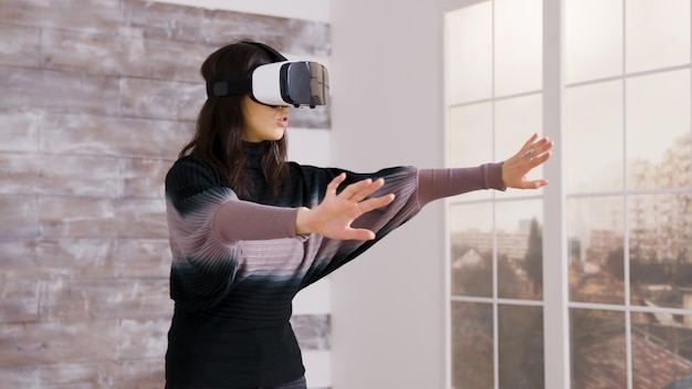 Hermosa diseñadora de casas usando gafas de realidad virtual dentro de un apartamento vacío.