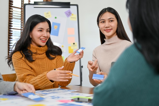 Hermosa diseñadora de interfaz de usuario asiática discutiendo y presentando su nuevo prototipo con su equipo