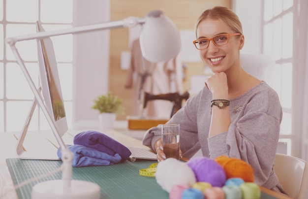 Hermosa diseñadora de moda sentada en el escritorio en el estudio