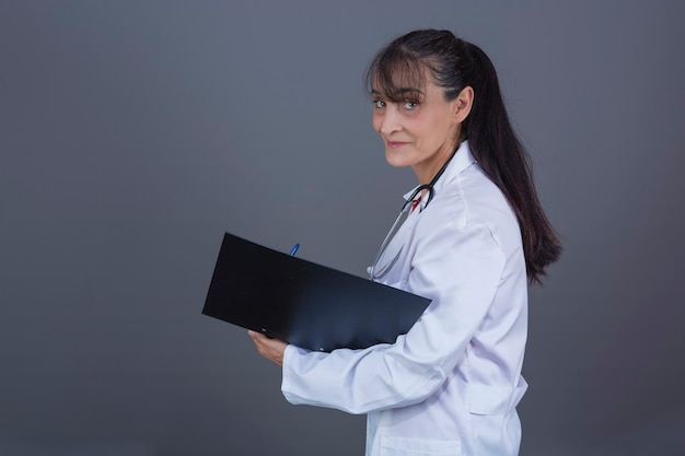 Hermosa doctora de unos 40 años con una carpeta de pelo largo en el lado de la mano mirando a la cámara