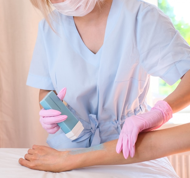 Hermosa doctora en un abrigo azul elimina el vello con cera