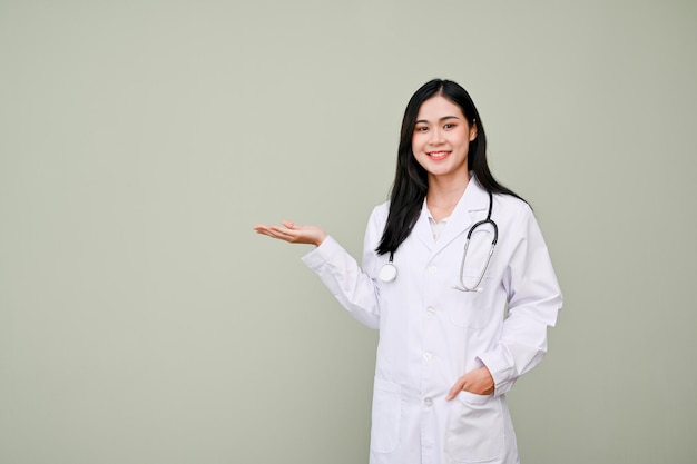 Hermosa doctora asiática palma abierta mirando a la cámara de pie contra el fondo gris