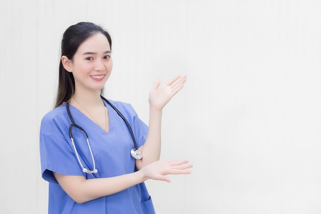 Una hermosa doctora asiática con uniforme azul se para y sonríe mientras apunta hacia la parte superior