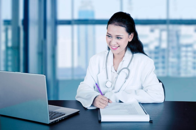 Hermosa doctora escribiendo en el portapapeles en el hospital