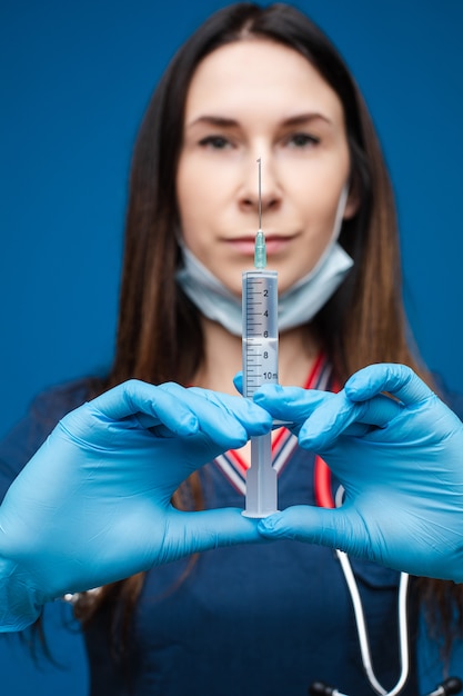 Hermosa doctora en ropa médica blanca, máscara, guantes azules y fonendoscopio sobre sus hombros