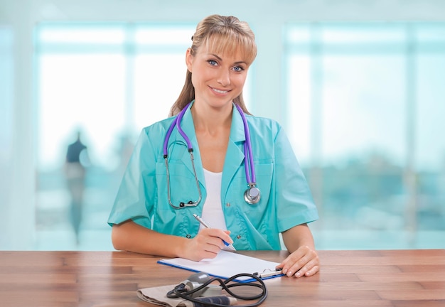 Hermosa doctora sentada en la mesa y escribiendo en el portapapeles