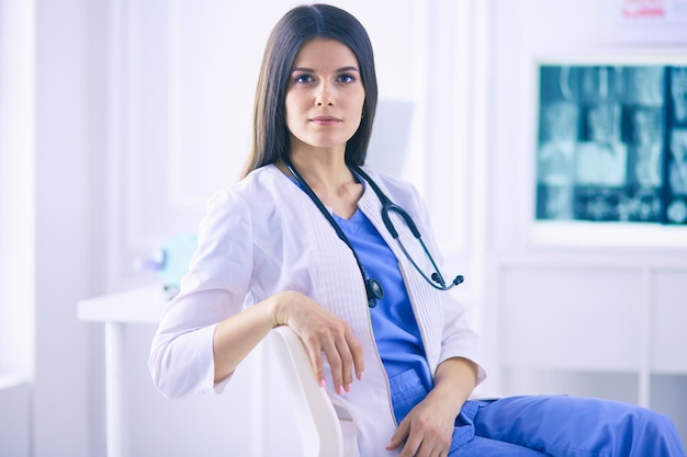 Hermosa doctora sentada en una sala de consulta sonriendo a la cámara