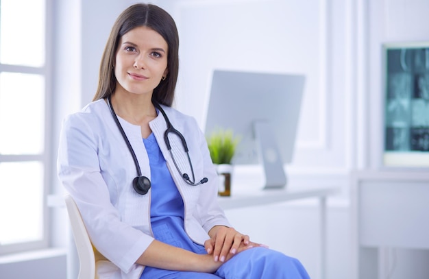 Hermosa doctora sentada en una sala de consulta sonriendo a la cámara