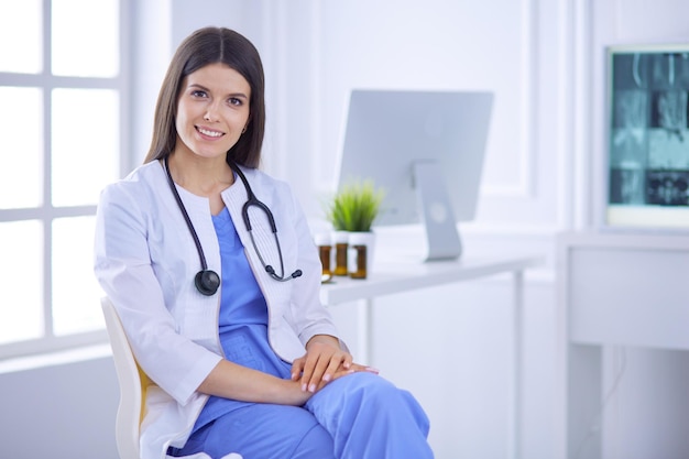 Hermosa doctora sentada en una sala de consulta sonriendo a la cámara