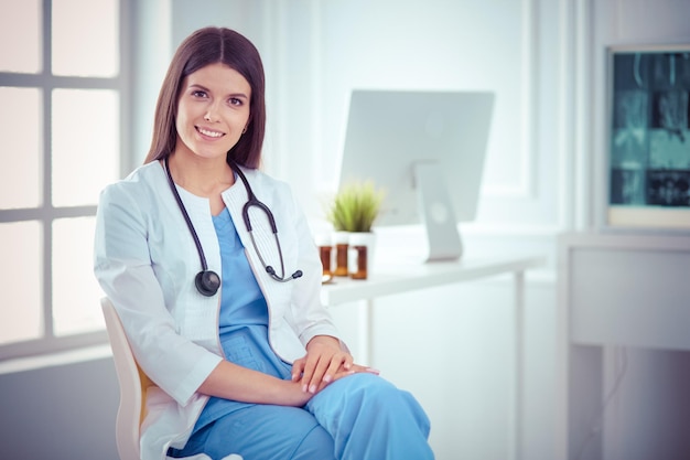 Hermosa doctora sentada en una sala de consulta sonriendo a la cámara