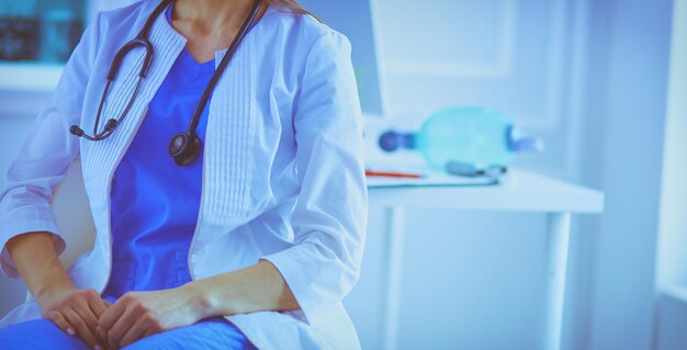 Hermosa doctora sentada en su lugar de trabajo en una sala de consulta sonriendo a la cámara