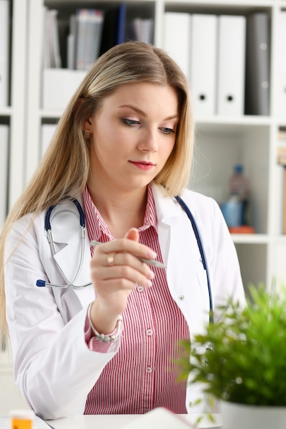 Hermosa doctora sonriente sentarse en el lugar de trabajo