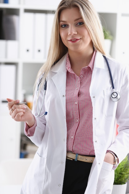 Hermosa doctora sonriente sentarse en el lugar de trabajo