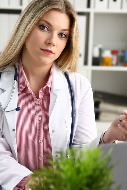 Hermosa doctora sonriente sentarse en el lugar de trabajo