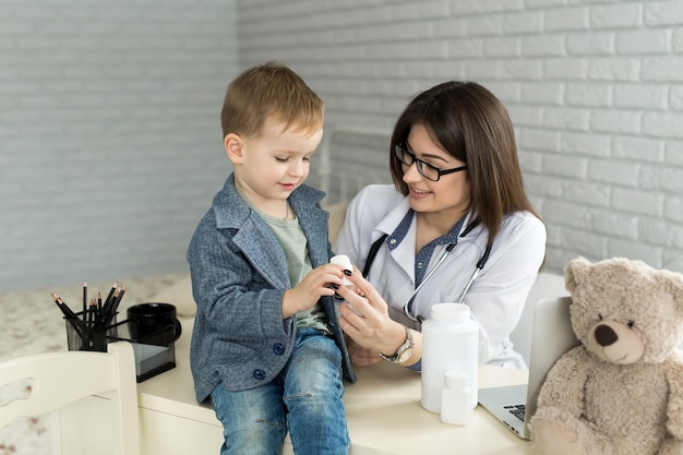 Hermosa doctora sonriente sostenga en frasco de pastillas de brazos y se lo ofrezca al primer visitante infantil.