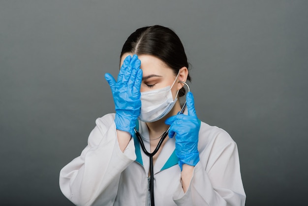 Hermosa doctora sosteniendo un estetoscopio y sonriendo aislado en gris.