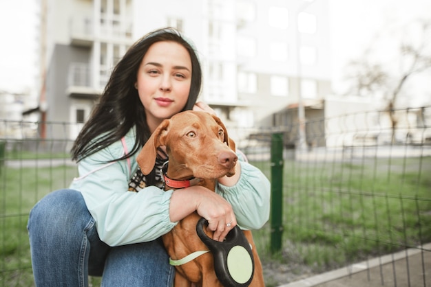 Hermosa dueña abraza a un lindo perro de raza marrón magyar vizsla y mira a la cámara