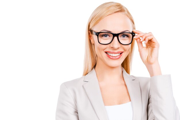 Hermosa e inteligente. Confianza empresaria madura ajustando sus gafas y sonriendo mientras está de pie contra el fondo blanco.