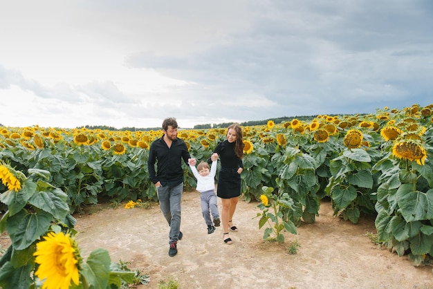 Una hermosa y elegante familia camina en un campo de girasoles Estilo de vida de verano al aire libre Ocio familiar con un niño