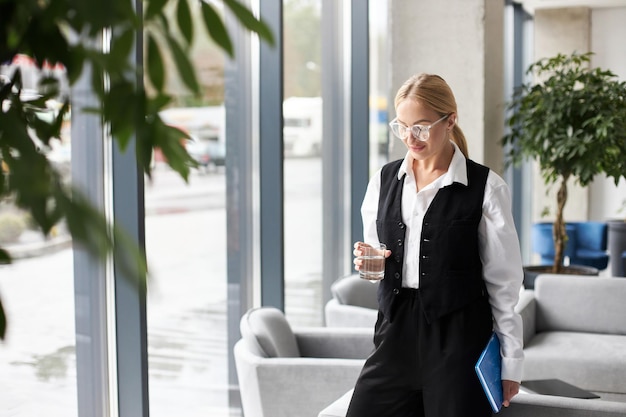 Hermosa y elegante mujer de negocios sosteniendo un vaso de agua en una oficina moderna