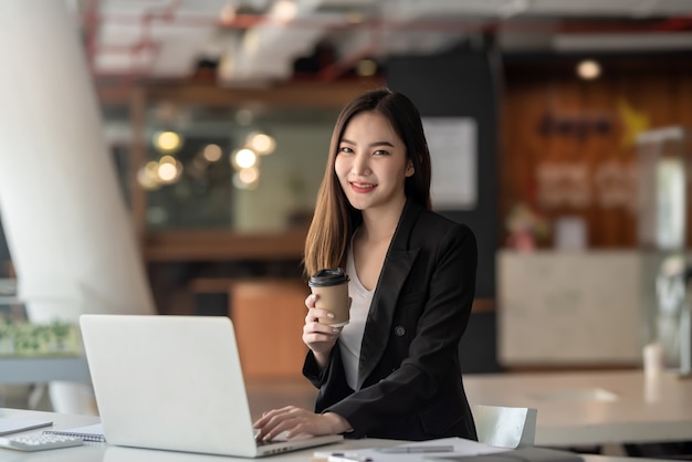 Hermosa empresaria asiática mirando a la cámara sosteniendo una taza de café en la oficina.