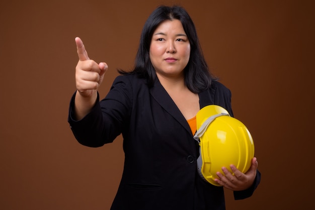 Hermosa empresaria asiática con sobrepeso sosteniendo hardhat en marrón