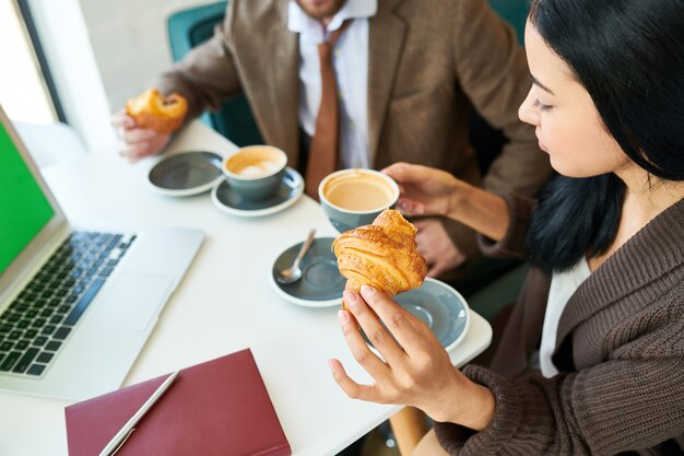 Hermosa empresaria disfrutando de café con croissant en el desayuno