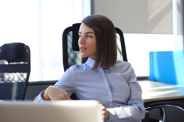 Hermosa empresaria está sentada en la oficina y mirando por la ventana.