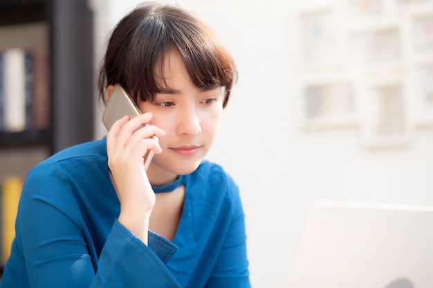 Hermosa empresaria joven asiática emocionada y contenta de éxito trabajar con la computadora portátil, chica tomando teléfono móvil inteligente