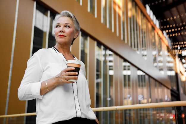 Hermosa empresaria de mediana edad con una taza de café posando en el interior del centro de negocios.