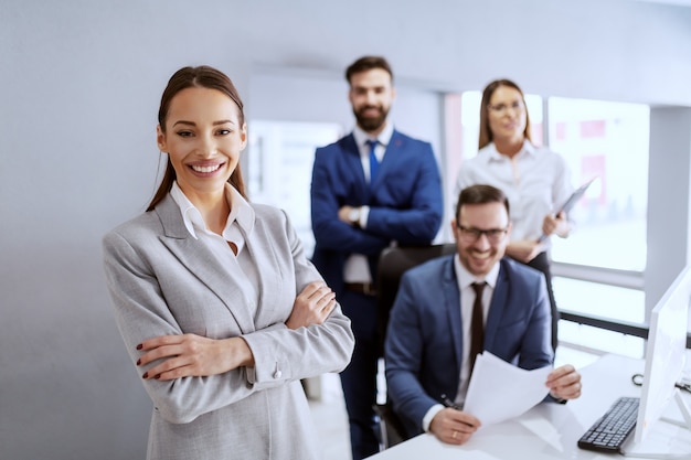 Hermosa empresaria sonriente en traje de pie en la oficina con las manos cruzadas.