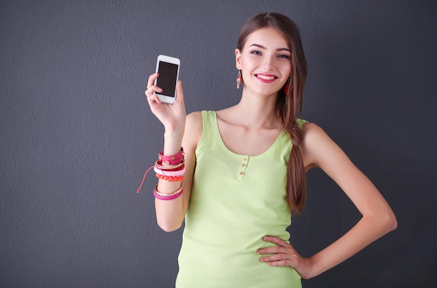 Hermosa empresaria con teléfono celular de pie junto a la pared