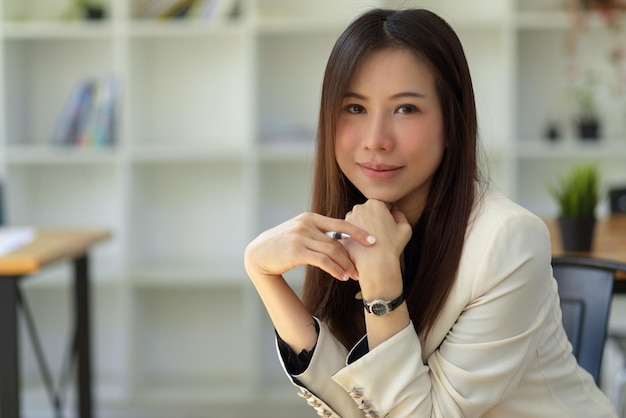 Hermosa y encantadora mujer de negocios asiática con traje blanco sentada y publicando en su lugar de trabajo