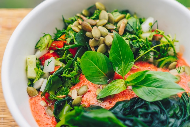 Hermosa ensalada crudivegana de hojas verdes mezclar verduras en plato blanco Receta de cocina Mezcla de tomate zanahoria coliflor corte perejil cilantro eneldo verdor pepino albahaca semillas de calabaza algas