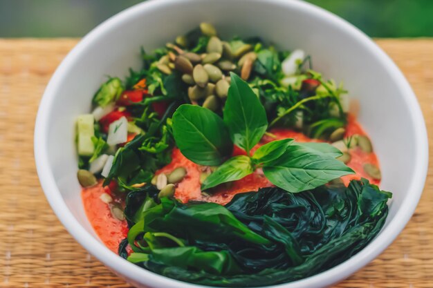 Hermosa ensalada crudivegana de hojas verdes mezclar verduras en plato blanco Receta de cocina Mezcla de tomate zanahoria coliflor corte perejil cilantro eneldo verdor pepino albahaca semillas de calabaza algas