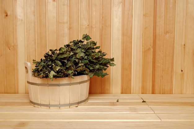 Hermosa escoba de baño grande acostado en un balde de madera redondo de pie sobre un banco en la sauna
