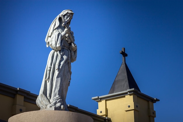 Foto hermosa estatua de santa rita de cassia con torre de iglesia y cielo azul al fondo