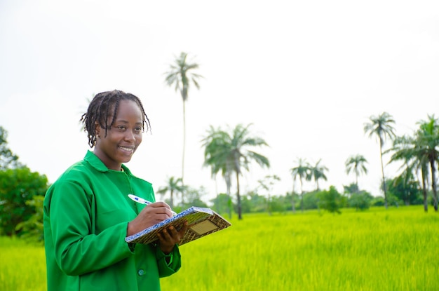 Hermosa estudiante africana en la granja tomando notas sobre sus resultados en la granja