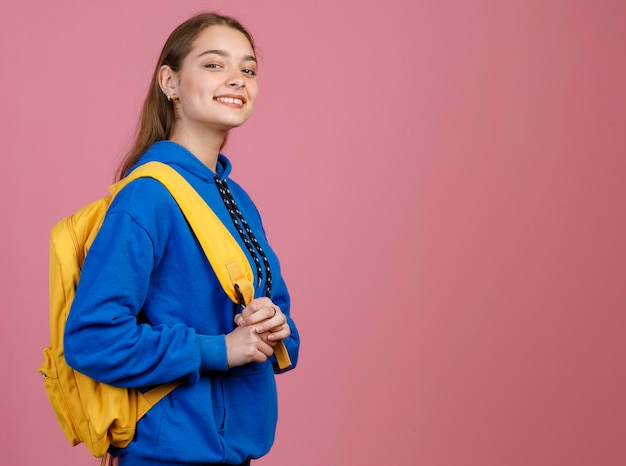 Hermosa estudiante alegre con mochila en el hombro sosteniendo una correa amarilla mientras posa