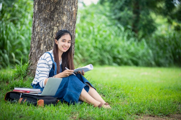 Hermosa estudiante asiática con libros y sonriendo y aprendiendo y concepto de educación en el parque en verano para relajarse