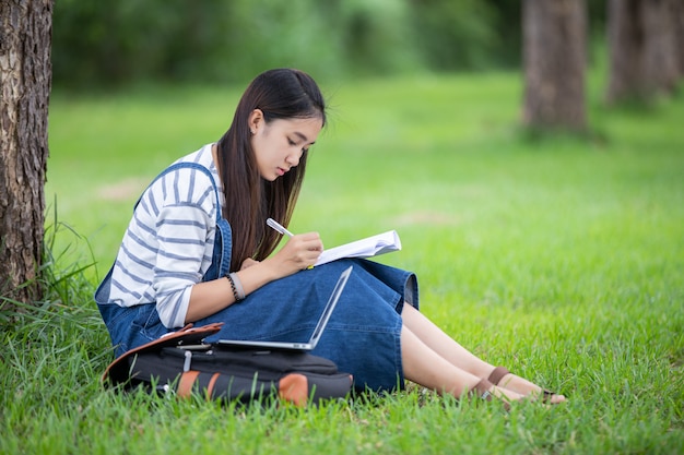 Hermosa estudiante asiática con libros y sonriendo y aprendiendo y educando en el parque en verano para relajarse