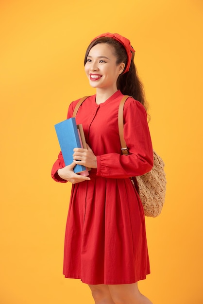 Hermosa estudiante asiática sosteniendo libros y trayendo una bolsa sobre fondo naranja