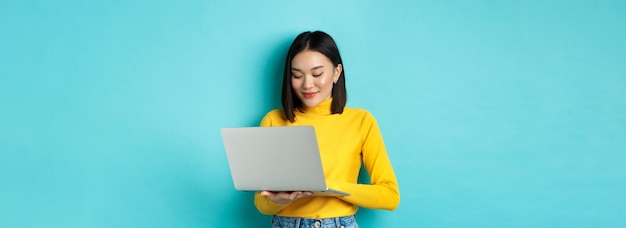 Hermosa estudiante asiática trabajando en una computadora portátil escribiendo en el teclado y mirando la pantalla con súplicas