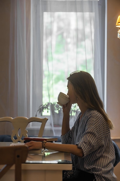 Hermosa estudiante bebiendo café en la cafetería y leyendo un libro durante el desayuno