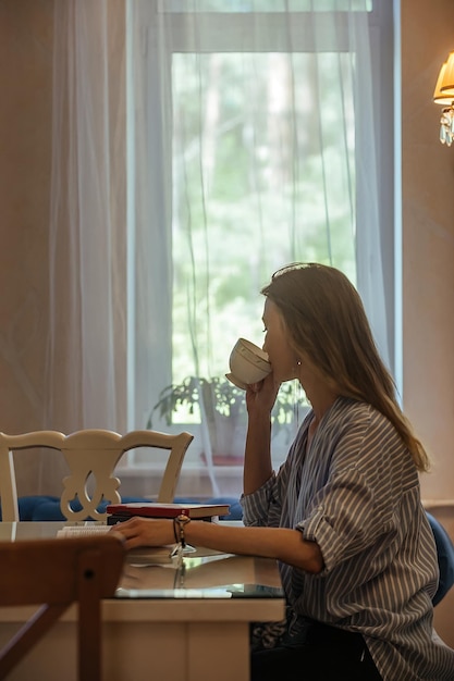 Hermosa estudiante con cabello largo bebe café en la cafetería y lee