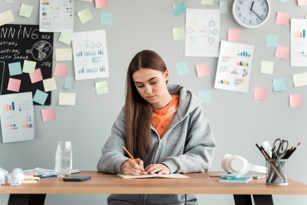 Foto hermosa estudiante estudiando en un escritorio sobre un fondo de una pared gris.